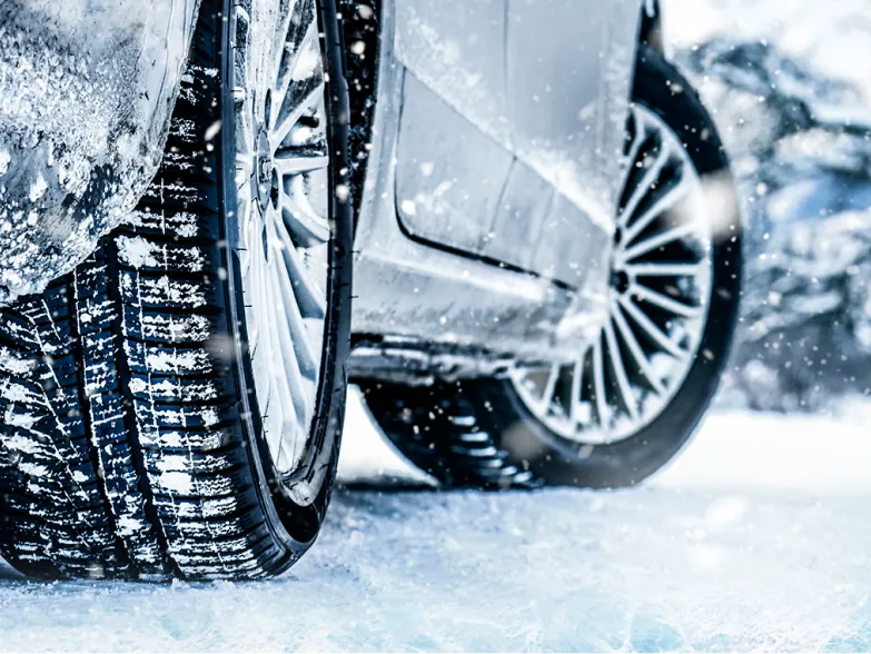 Nahaufnahme eines Autoreifens mit tiefem Profil auf einer verschneiten Fahrbahn bei Schneefall.